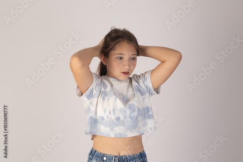 Young girl is posing for a photo with her hands behind her head.