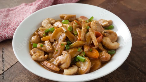 Delicious stir-fried chicken and shrimp with vegetables in a white ceramic bowl garnished with green onions shot in a kitchen setting with warm natural light and a wooden table background