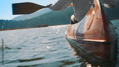 A person paddles a canoe on a serene lake, surrounded by forested mountains. The scene captures tranquility and adventure, ideal for outdoor enthusiasts and those seeking a peaceful retreat.