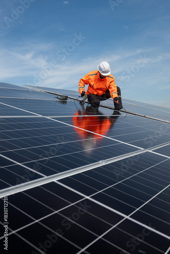Technician installing solar panels on factory roof for green energy. A skilled technician in safety gear is working on a solar panel installation on rooftop.