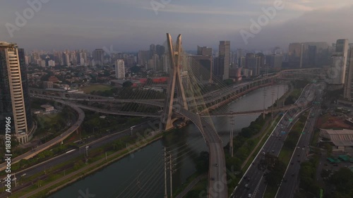 aerial view of a cable stayed bridge in Sao Paulo city during sunset with skyscrapers, traffic and a river