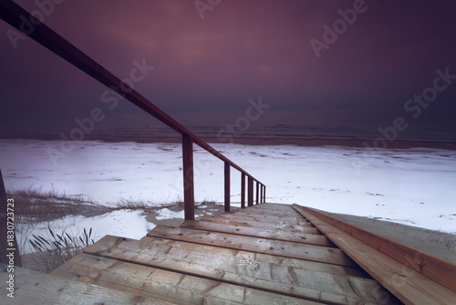 Fototapeta Naklejka Na Ścianę i Meble -  Vibrant Baltic Sea Winter Sunset with wooden ladders pathway to the sandy beach in Lithuania