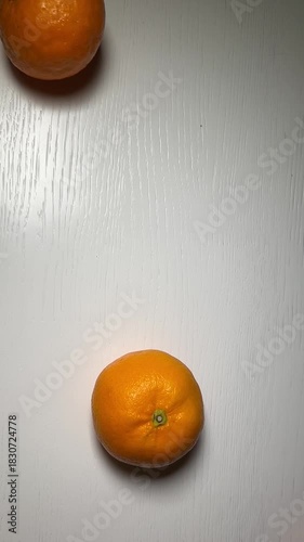 Tangerines rolling one by one on a white table, top view. Minimalistic natural motion.