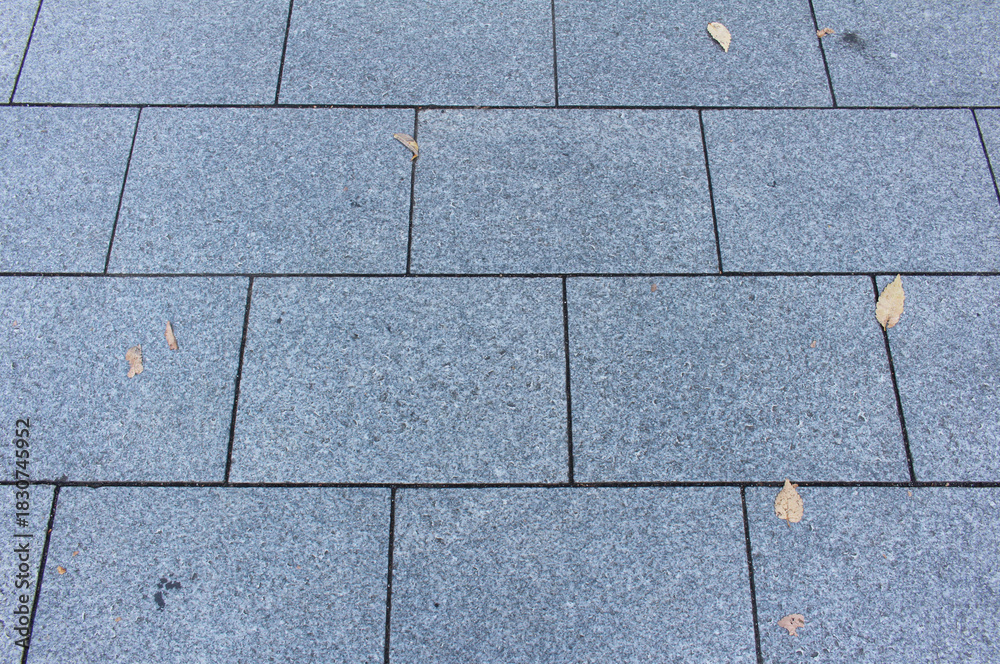 Fototapeta premium Texture of square paving tile. Pattern of blue tiles in the street. Concrete pavers with autumnal leaves close up background.