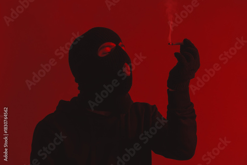 Man in Hoodie and Black Balaclava Closing Eyes While Holding a Lit Cigarette