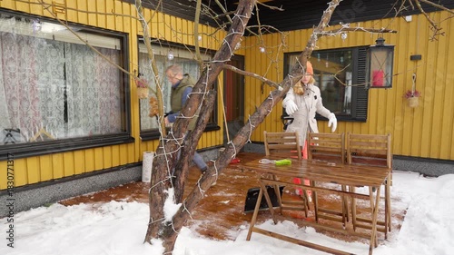 Happy winter lifestyle moment as a couple clears fresh snow from a cozy home patio. Cold weather, soft daylight, teamwork and seasonal mood create a warm family atmosphere.