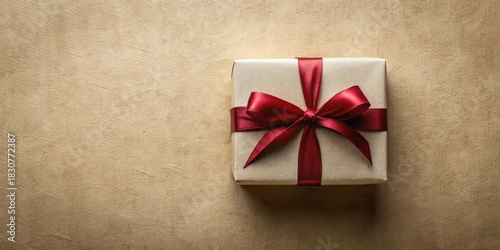 A single elegantly wrapped present with a deep crimson ribbon bow sits atop textured kraft paper, suggesting a thoughtful gift and anticipation of joyous occasion