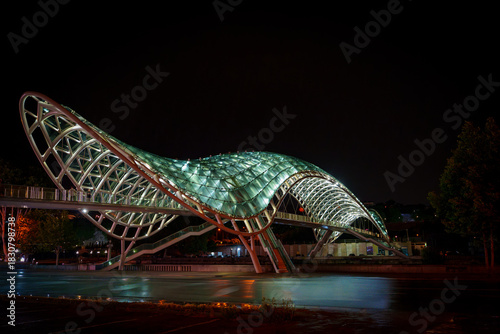 Illuminated Peace Bridge spanning Kura River in Tbilisi at night