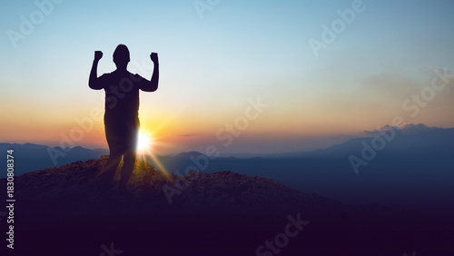 Silhouette of a person standing on a hilltop with arms raised in celebration against the sunrise background. Concept of a winner