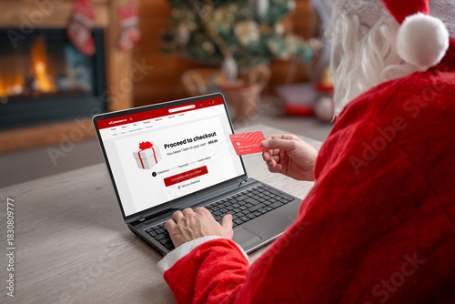 Santa completing online checkout on laptop with credit card in warm Christmas interior, ideal for ecommerce themes, holiday shopping promotions and seasonal marketing