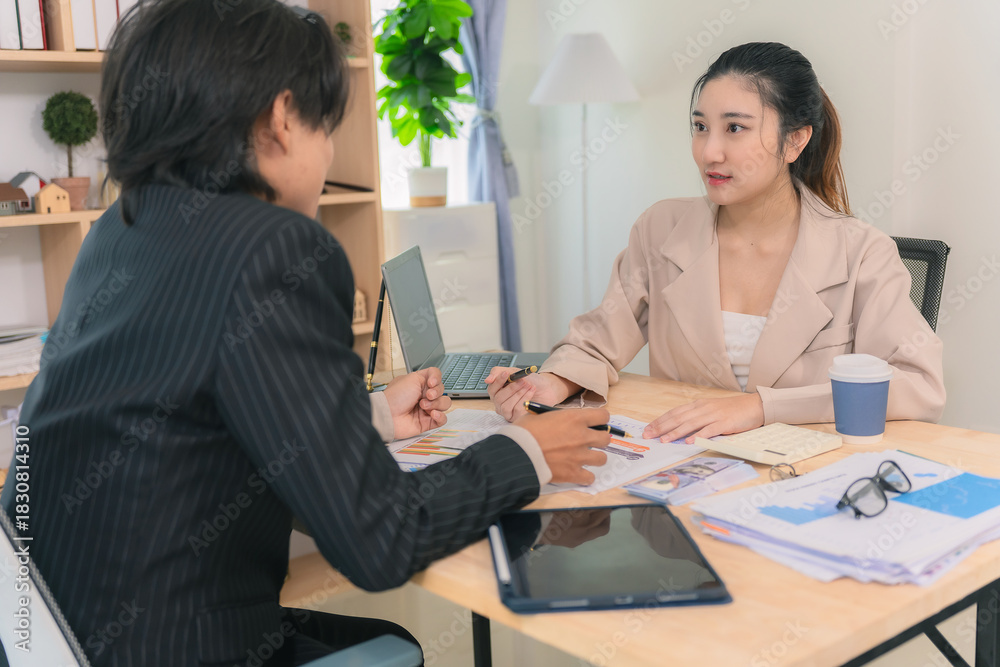 Fototapeta premium Asian business couple discussing finances over documents and laptop, explaining details of business growth chart.