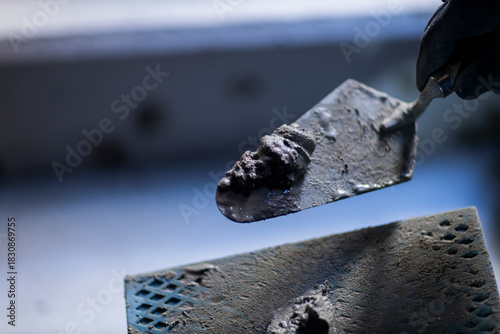 Close-up of a construction trowel holding fresh cement mortar. The image focuses on building materials and manual construction work.