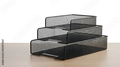 Stacked, black, wire-mesh desk trays on a light wood surface, against a white background