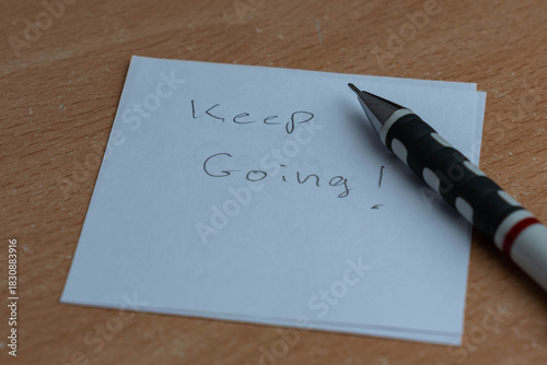 White  note with Keep Going text with a pencil close up shot.