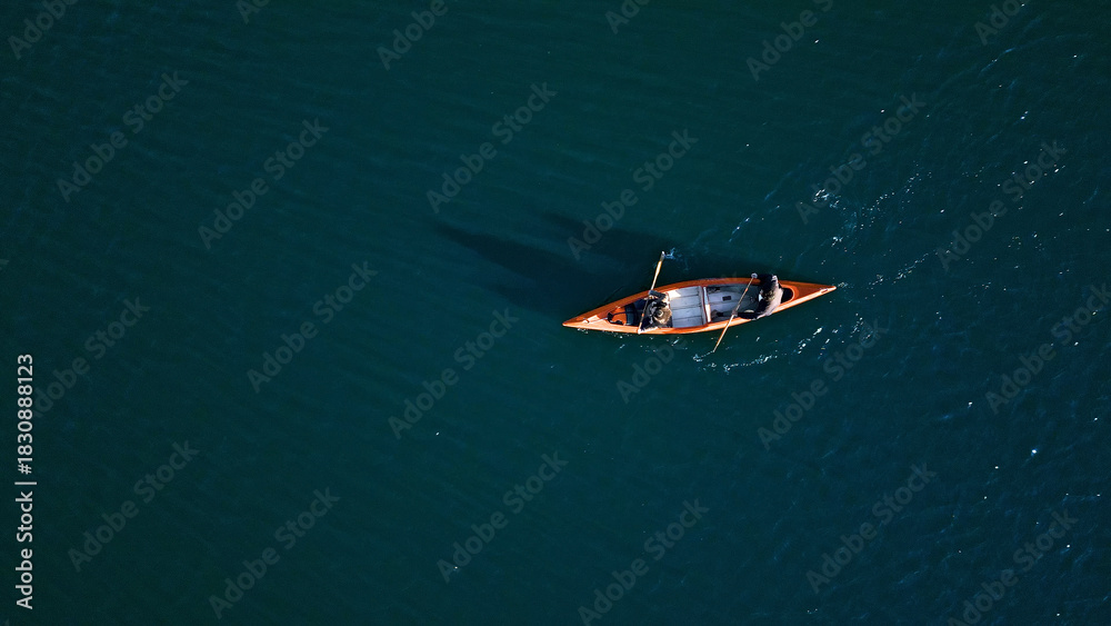 Fototapeta premium A couple paddles a canoe on a serene, deep blue lake, embodying a weekend escape into nature. The tranquil setting, captured with an aerial shot, highlights their active lifestyle and connection.