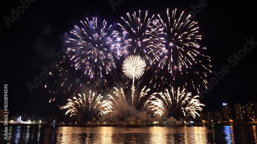 Colorful explosions illuminate night sky over water reflecting light