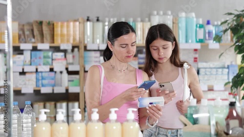 Attentive focused mother and daughter buyers scanning qr code for box of ointment or gel in small pharmacy