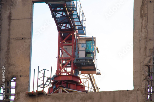 Close-up view of Control Cabin of Red-and-white Tower Crane on Construction Site against Blue Sky on Sunny Day. View through the Opening of Monolithic Box Window.