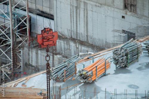 Red Rusty Hook suspension Tower Crane against background Warehouse of Yellow Volumetric I-Beams Formwork on Roof Monolithic Building Box. Background Construction Site with Rebar outlet Concrete Walls.