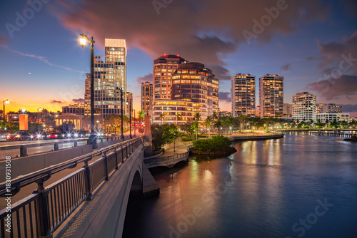 West Palm Beach, Florida, USA. Cityscape image of West Palm Beach, Florida with bridge leading to the downtown and reflection of the city skyline in the water at beautiful sunset.