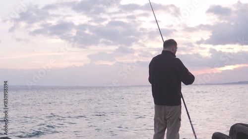 A man with a fishing rod is standing by the seashore and fishing