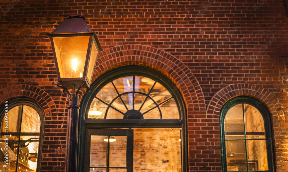 Fototapeta premium Vintage street lantern glowing against historic brick architecture in the Distillery District of Toronto, Canada, captured during the evening.