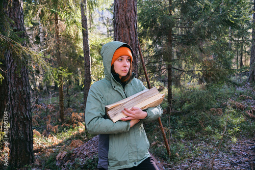 A young woman carries firewood in her hands in the forest. The concept of preparing firewood for the winter
