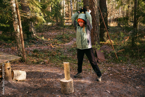 A young woman is chopping wood with an axe in the forest. The concept of preparing firewood for the winter stove.