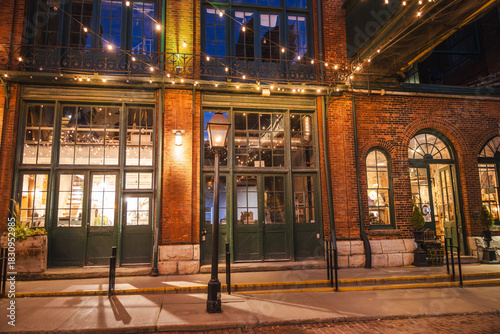 Photography Historic brick storefronts illuminated by warm lights in the Distillery District of Toronto during the evening
