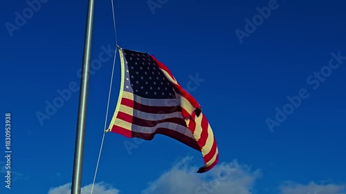 waving American flag on a tall flagpole stretches against a clear blue sky, symbolizing patriotism, freedom, and national pride