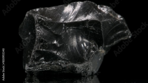 Obsidian - black silica-rich volcanic glass formed by rapidly-cooled viscous lava - revolving slowly against a black background