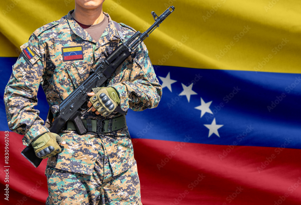 Obraz premium Venezuela flag with soldier in military uniform holding assault rifle in front of it
