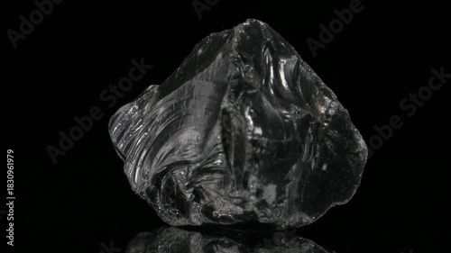 Obsidian - black silica-rich volcanic glass formed by rapidly-cooled viscous lava - revolving slowly against a black background