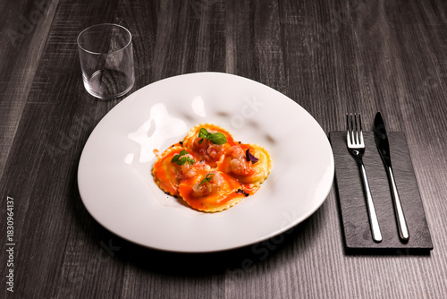 Piatto di ravioli freschi ripieni di tartare di gamberi, conditi con bische di gamberi e gamberi crudi usati come guarnizione servito in un ristorante elegante