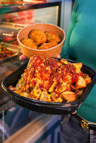 Porzione di patate al forno condite con maionese, ketchup e bacon croccante e una porzione di polpette fritte messe nei contenitori da asporto 