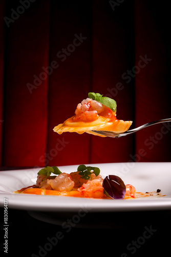 Piatto di ravioli freschi ripieni di tartare di gamberi, conditi con bische di gamberi e gamberi crudi usati come guarnizione servito in un ristorante elegante