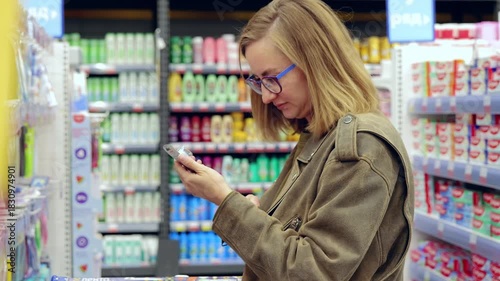 Young woman browsing supermarket aisles, comparing different toothpaste brands. Evaluating options for her oral care routine while selecting products
