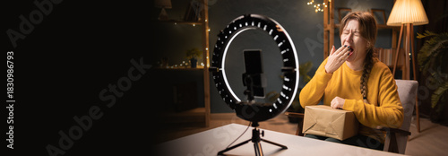 Female blogger unpacking box recording video using smartphone, ring light with tripod yawns with his hand over his mouth late evening at home office. online shopping and social media