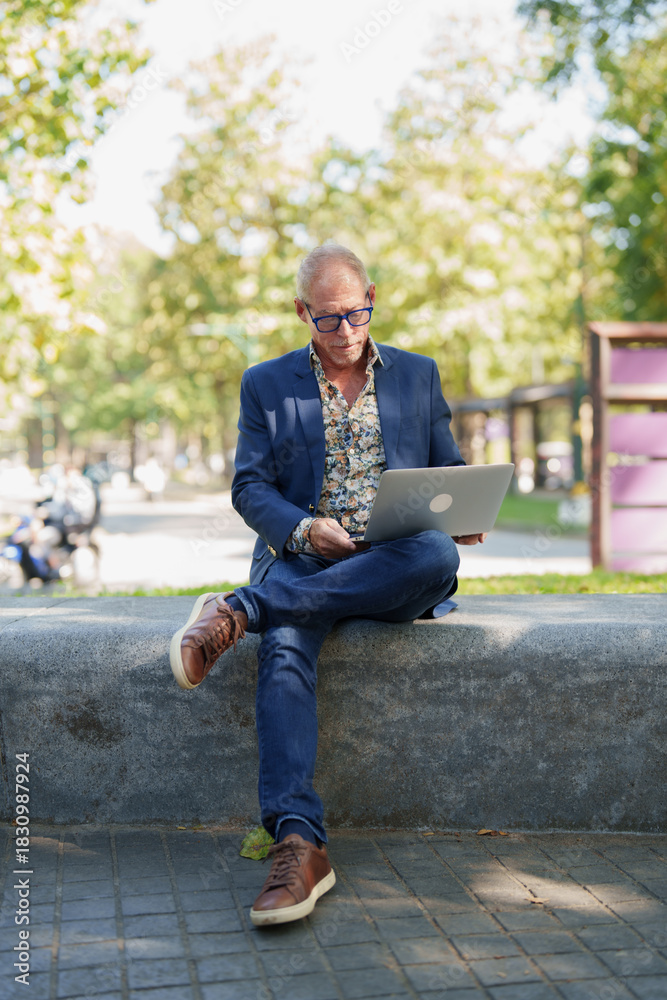 Obraz premium Senior man working outdoors on laptop in park