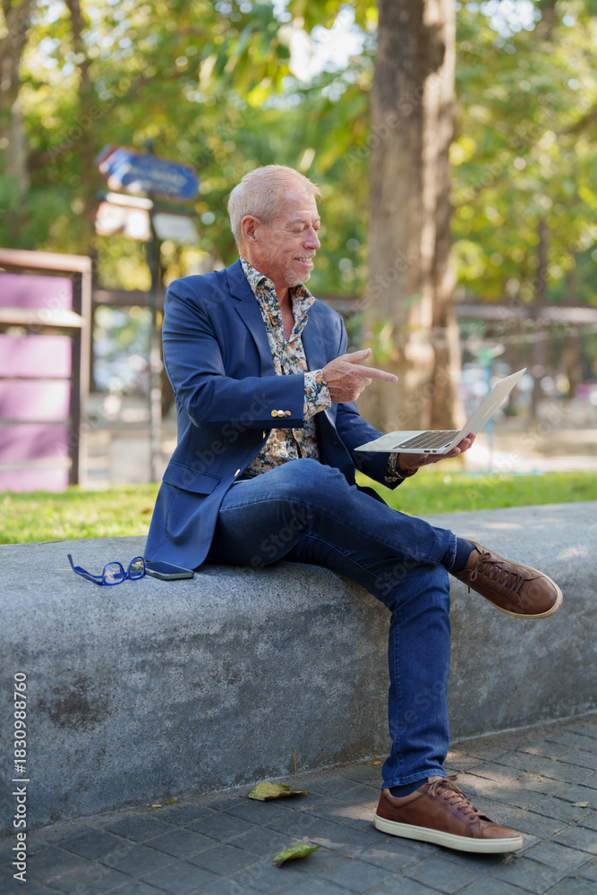Obraz premium Senior man smiling using laptop remotely outdoors