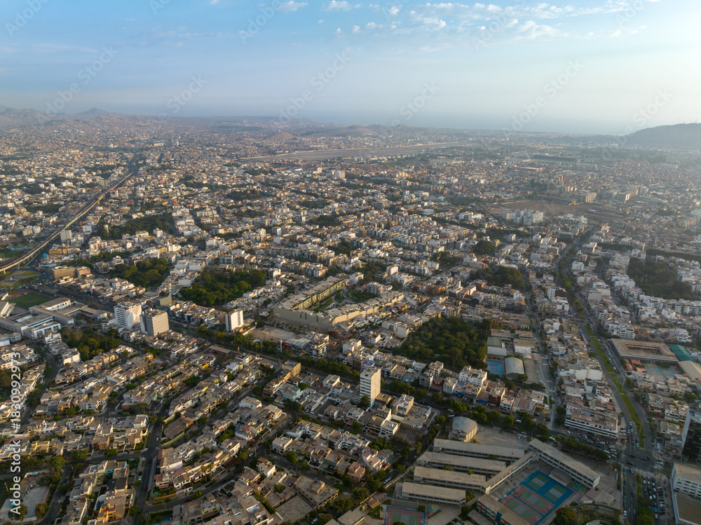 Naklejka premium Aerial view of the San Antonio neighborhood in Miraflores, Lima, showing the intersection of Benavides and La Merced avenues, surrounded by residential buildings and green areas at sunset.