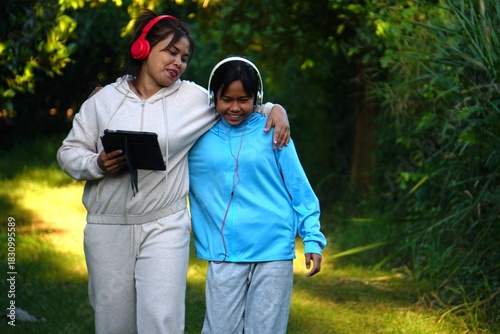 Mother and daughter walking side-by-side in the park, with the mother's arm around her daughter's shoulder, and the daughter smiling happily.