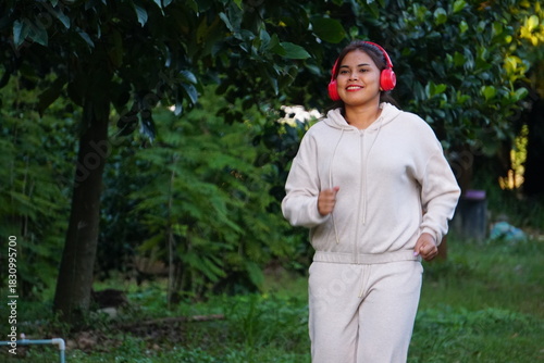 A woman (mother) is running/jogging alone in the park while wearing red headphones.
