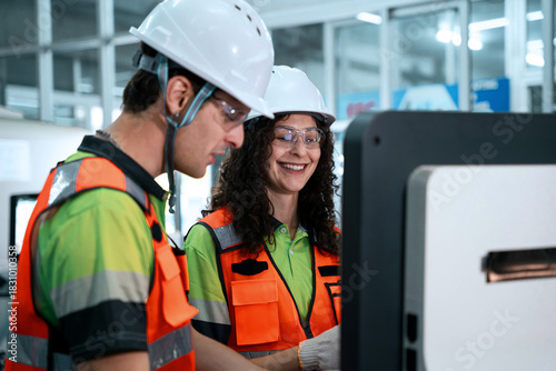 Two people wearing safety gear are looking at a computer screen
