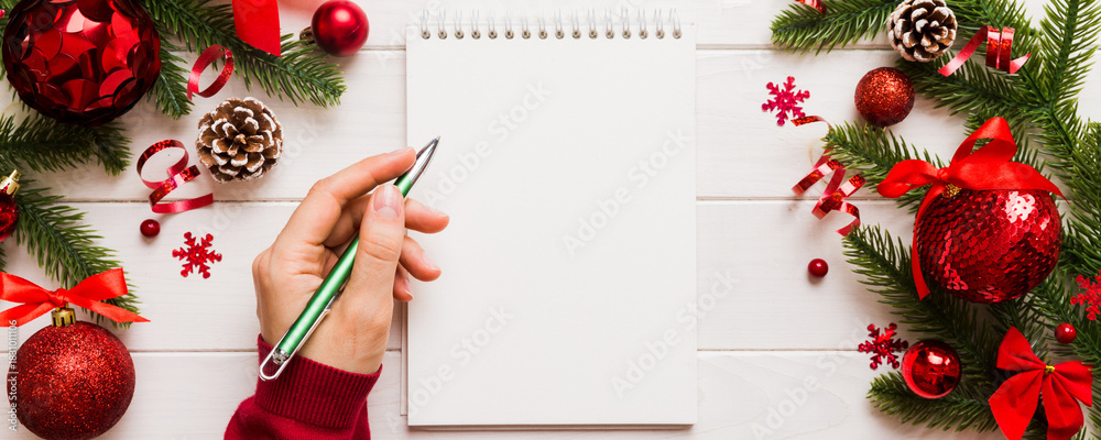 Fototapeta premium Woman writing Christmas to do list on notebook on colored background with xmas decorations