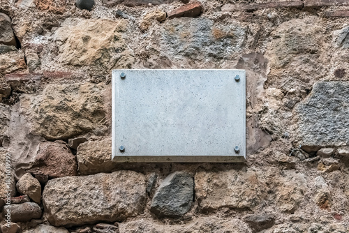 Blank marble plaque mockup mounted with steel bolts on an ancient textured stone wall. Empty plaque provides realistic space for customizable commemorative text or branding against weathered masonry