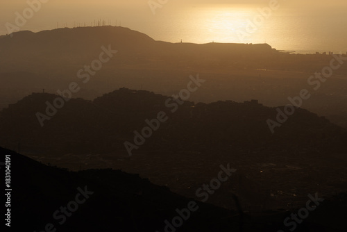 Hillside shantytown contrasting with a distant modern city skyline in the mist, illustrating social inequality, poverty, and urban sprawl in Lima, Peru