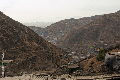 Hillside shantytown contrasting with a distant modern city skyline in the mist, illustrating social inequality, poverty, and urban sprawl in Lima, Peru