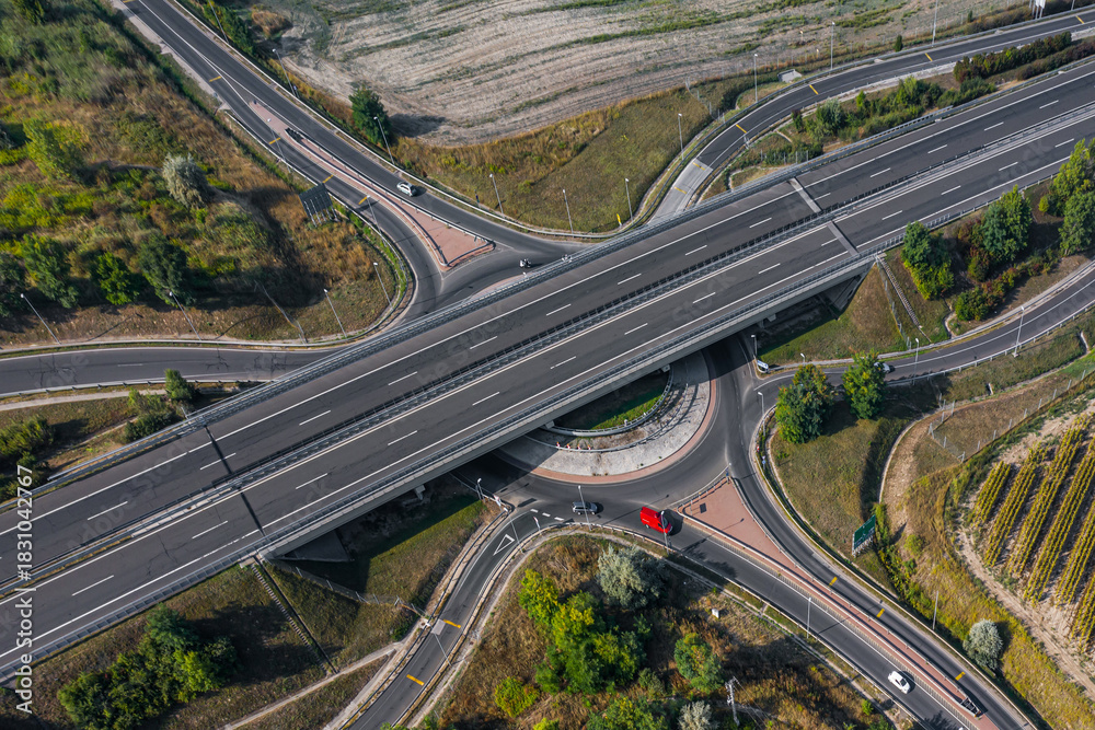 Fototapeta premium Daytime aerial view of a highway overpass and roundabout connection. Clean lines, modern infrastructure and smooth traffic routes.