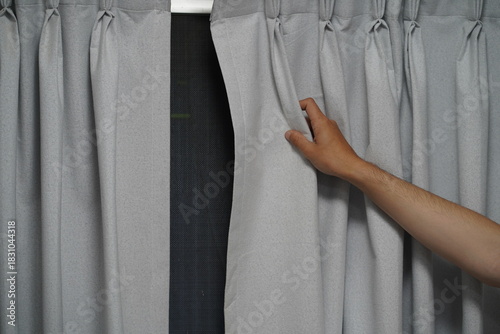 Person Opening Light-Gray Curtains to Reveal a Bright Window in a Cozy Interior Space with Natural Light Streaming In